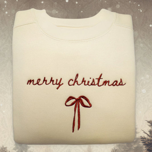 Folded beige sweatshirt with 'merry christmas' and a red bow on a snowy background