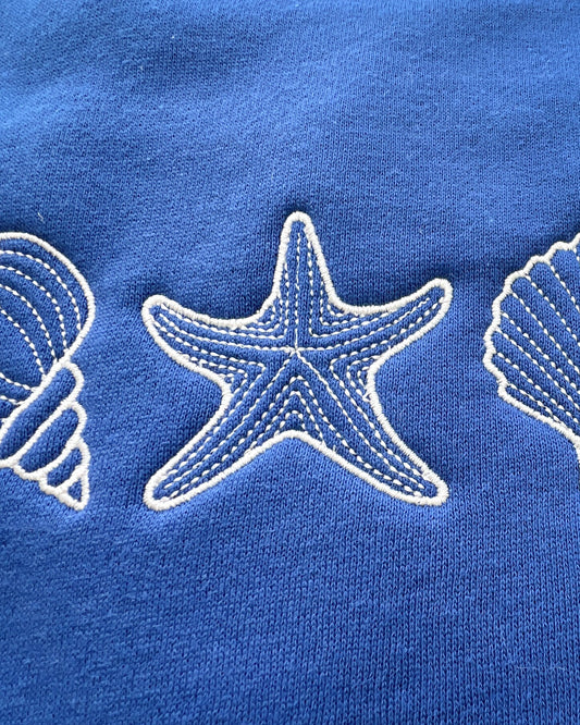 A blue sweatshirt with a design of seashells and a starfish on the front.